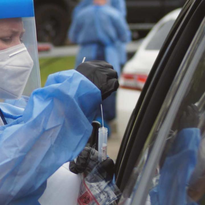 A nurse performing a nasal swab test through a car window.
